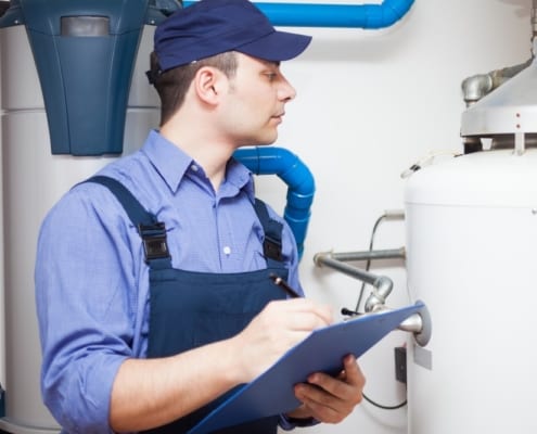 A man in blue overalls with a clip board looking at a residential water heater.