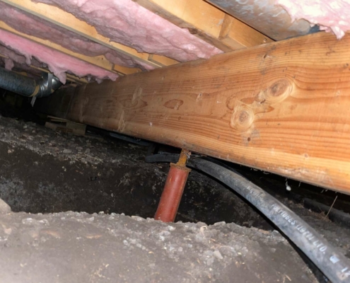 An outdated crawlspace with exposed dirt floor highlighting antiquated construction methods vulnerable to moisture issues.