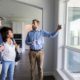 Confident home inspector shows potential homeowners the living room windows in the home.