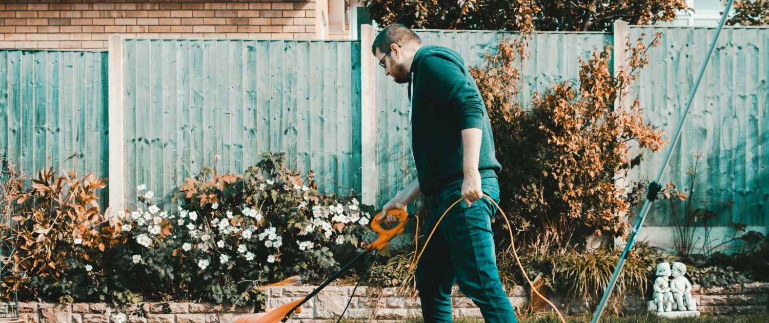 Manholding an orange electric grass trimmer on the lawn
