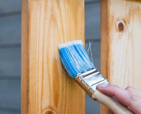 Hand holding a paint brush painting stain onto wood