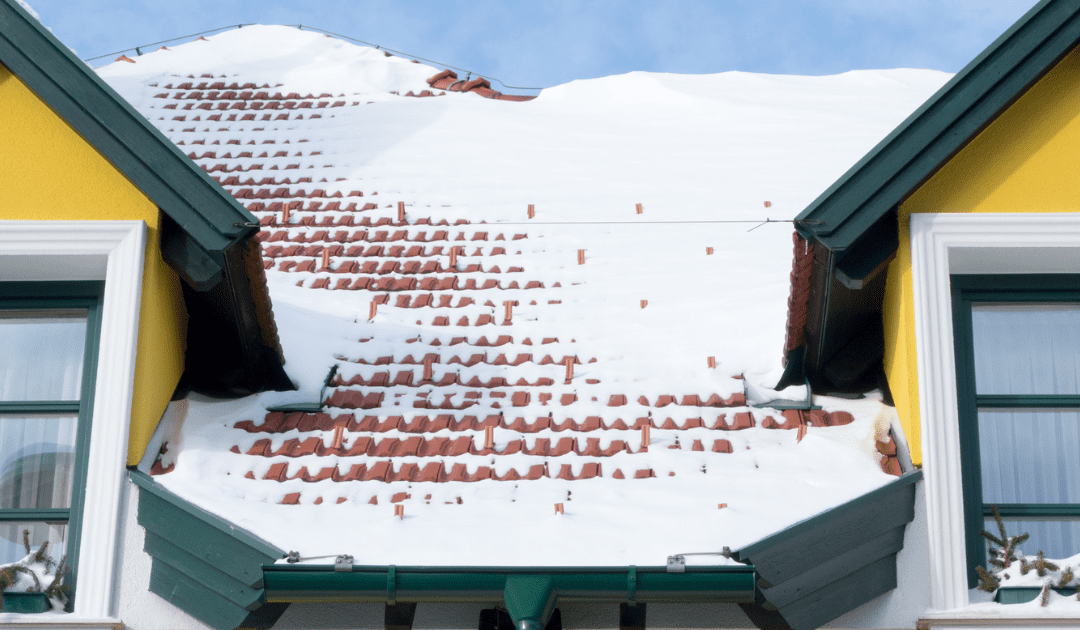 Snow-covered roof of a yellow house with green gutters.
