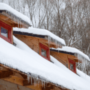 Snow and icicles on a wooden cabin roof with red windows.