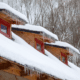 Snow and icicles on a wooden cabin roof with red windows.