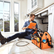 Plumber inspecting a sink pipe under a kitchen counter.