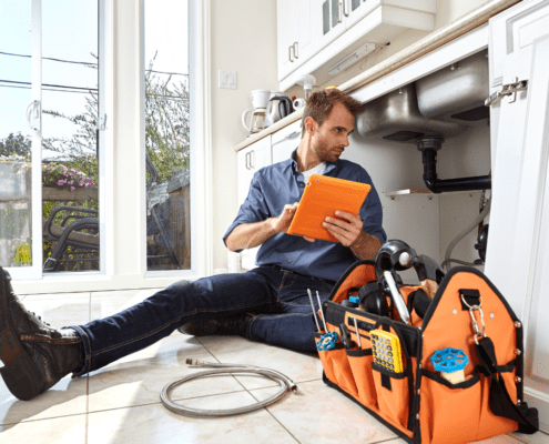 Plumber inspecting a sink pipe under a kitchen counter.