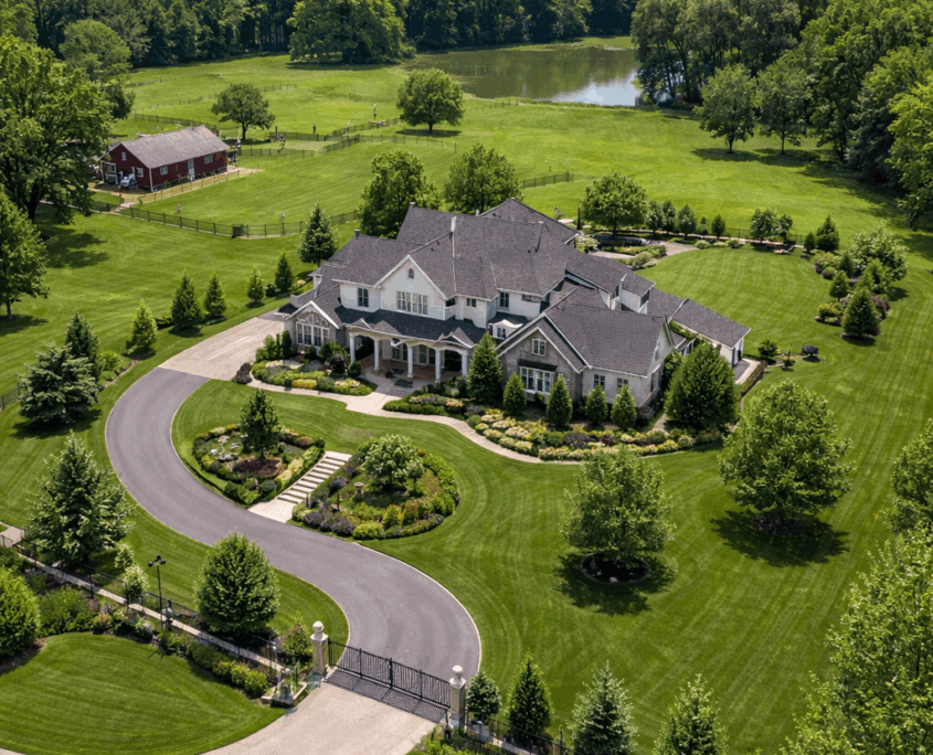 Aerial view of a rural acreage home with surrounding trees and open land, showing rooflines and property layout